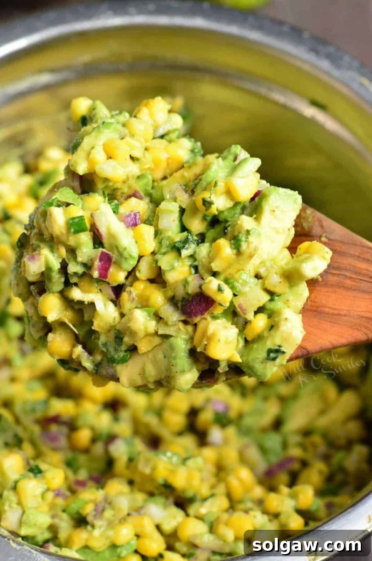 Vibrant Avocado and Sweet Corn Salad 4 A wooden spoon scooping out a generous portion of Avocado Corn Salad from a large white bowl, highlighting the colorful medley of ingredients.