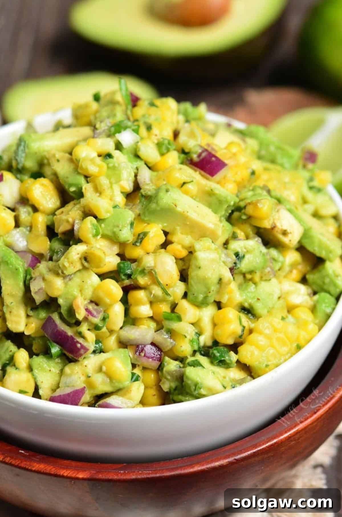 Avocado Corn Salad in a bowl with avocado sliced in half in the background.