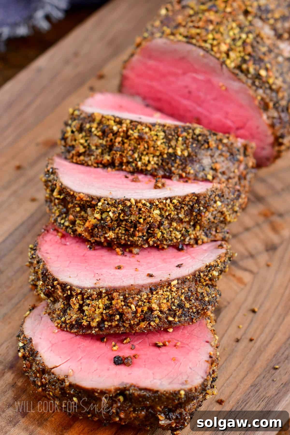 sliced beef tenderloin crusted in peppercorn seasoning on cutting board.