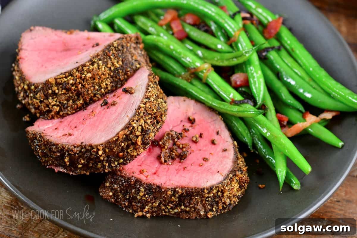 three slices of beef tenderloin overlapped next to green beans with bacon.
