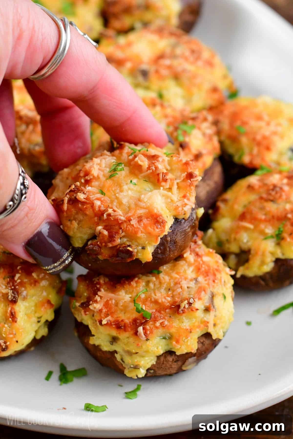 Decadent Mushroom Caps 6 A single stuffed mushroom cap held above a platter of others, garnished with green herbs.