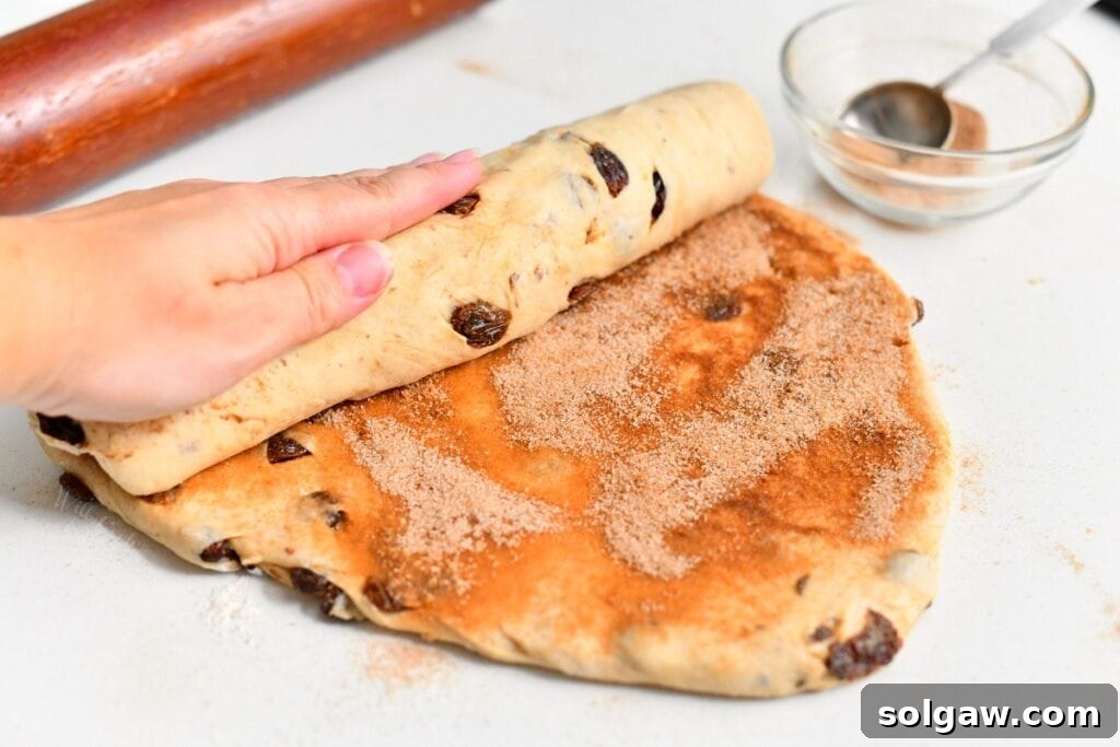woman's hand rolling bread dough with cinnamon sugar mixture