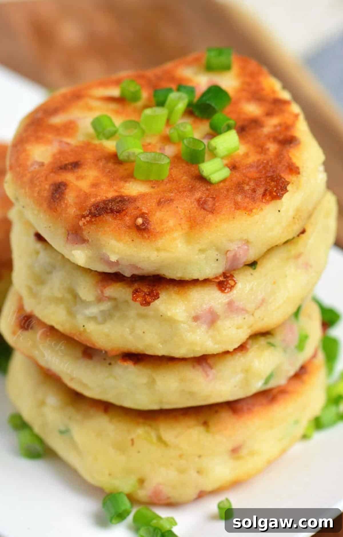 four mashed potato cakes with ham and cheese stacked and topped with chives.