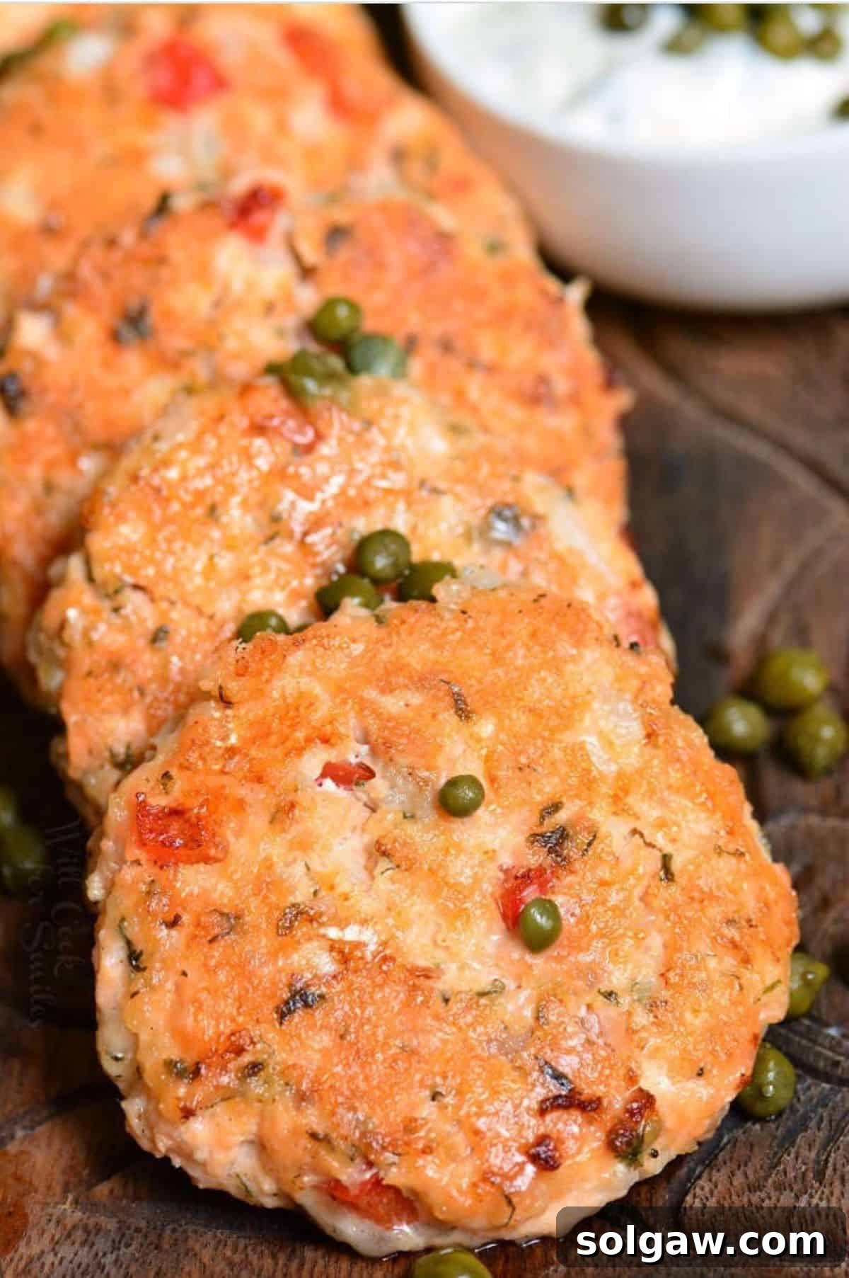 several salmon patties side by side on wooden plate with capers.