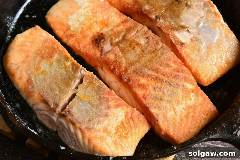 Searing salmon fillets in a hot cast iron pan with butter