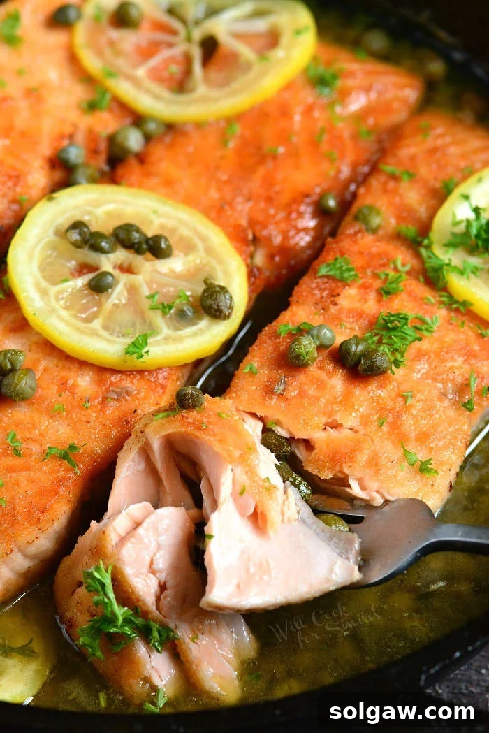 Salmon Piccata garnished with fresh parsley, lemon slices, and capers in a cast iron skillet