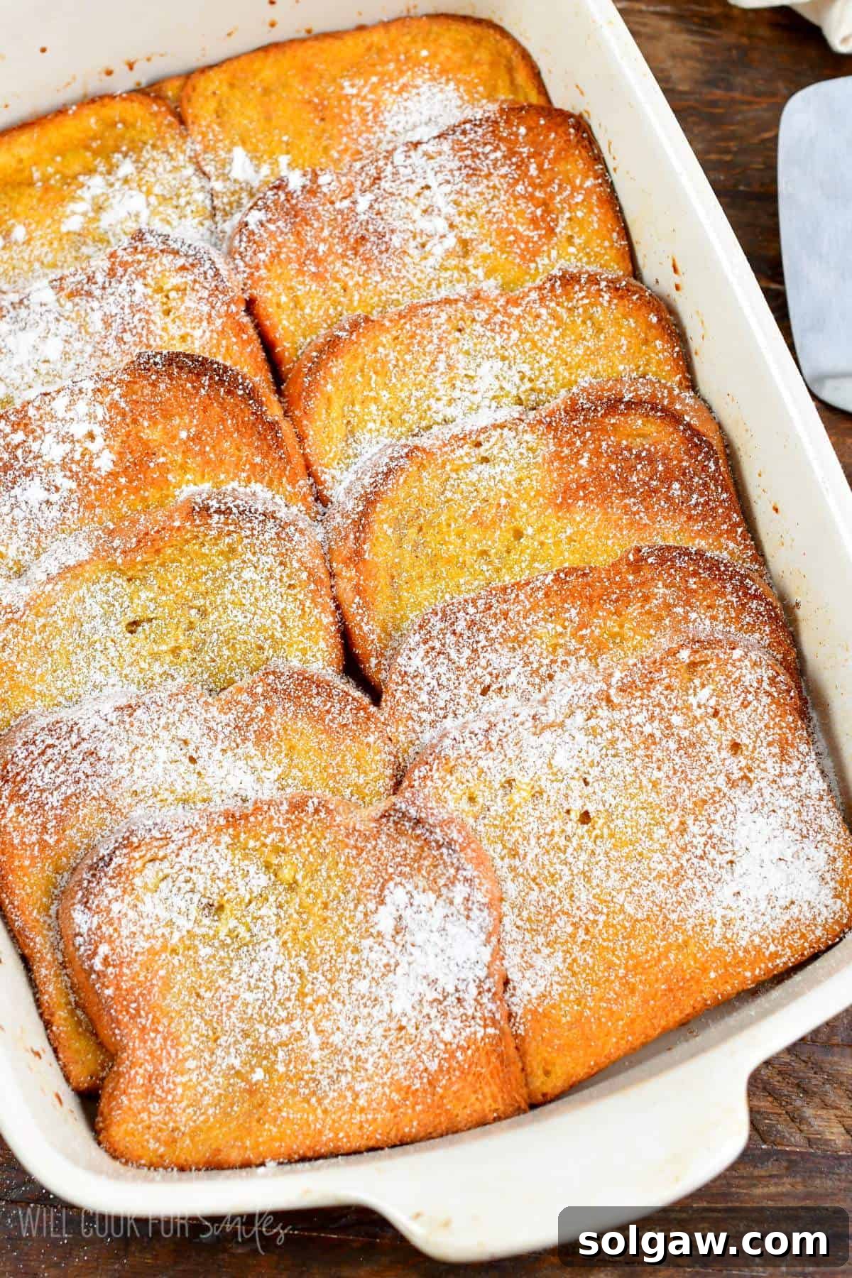 Baked French toast casserole in a white baking pan with powdered sugar. A perfect breakfast for holidays and family gatherings.