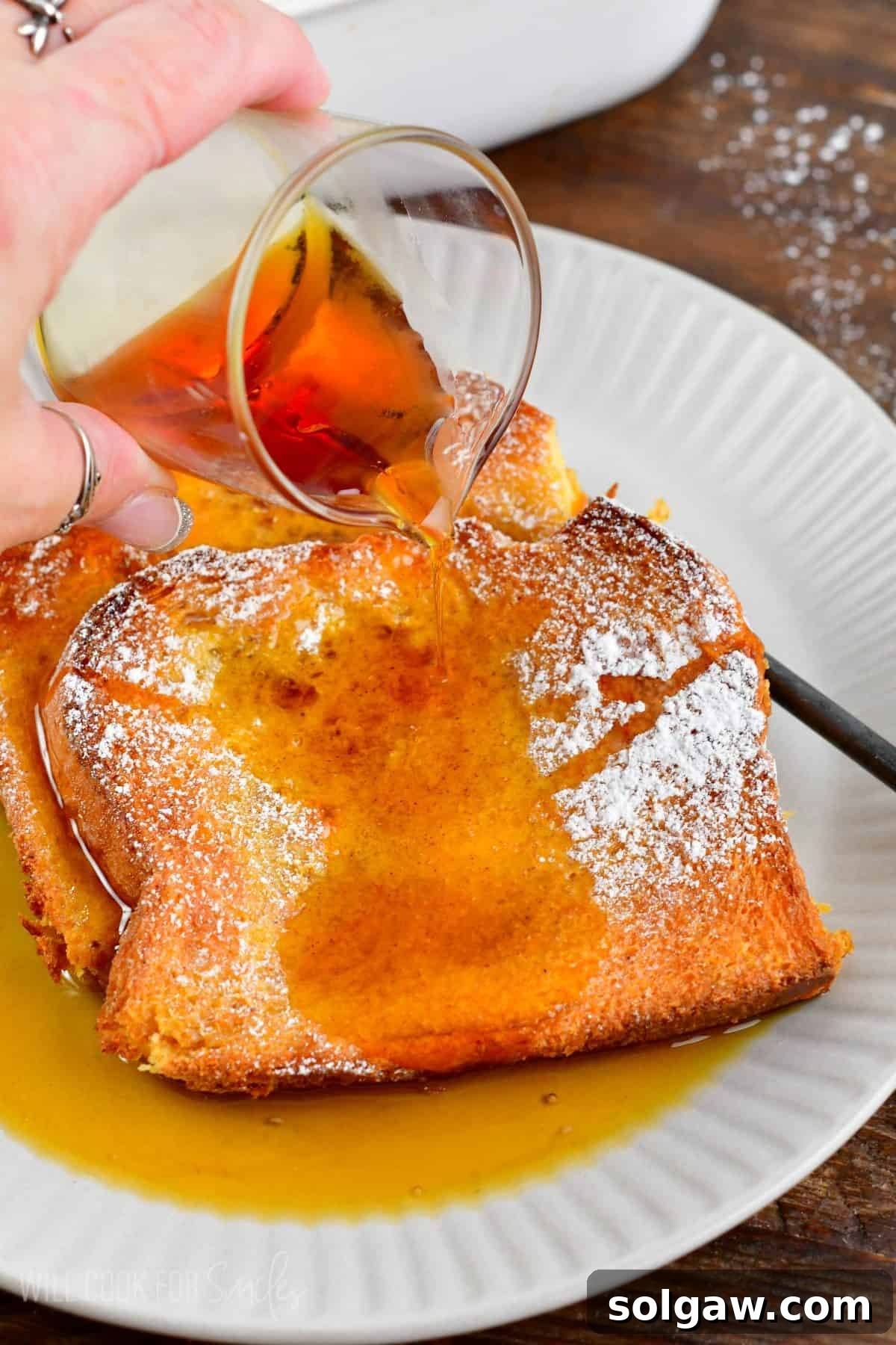 adding maple syrup to the slices of baked French toast on the plate.