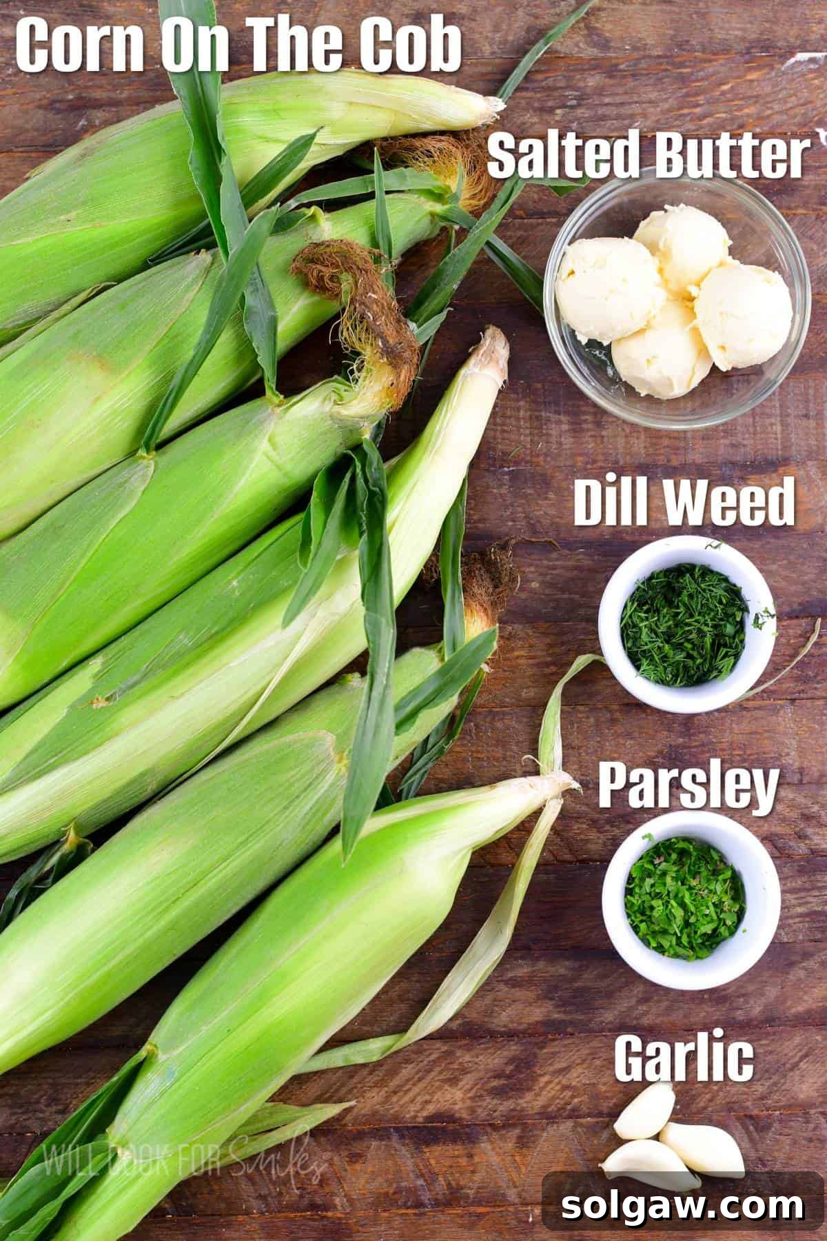 Labeled ingredients for grilled corn on the cob with garlic herb butter, including fresh corn, butter, parsley, dill, and garlic cloves, laid out on a rustic wooden board.