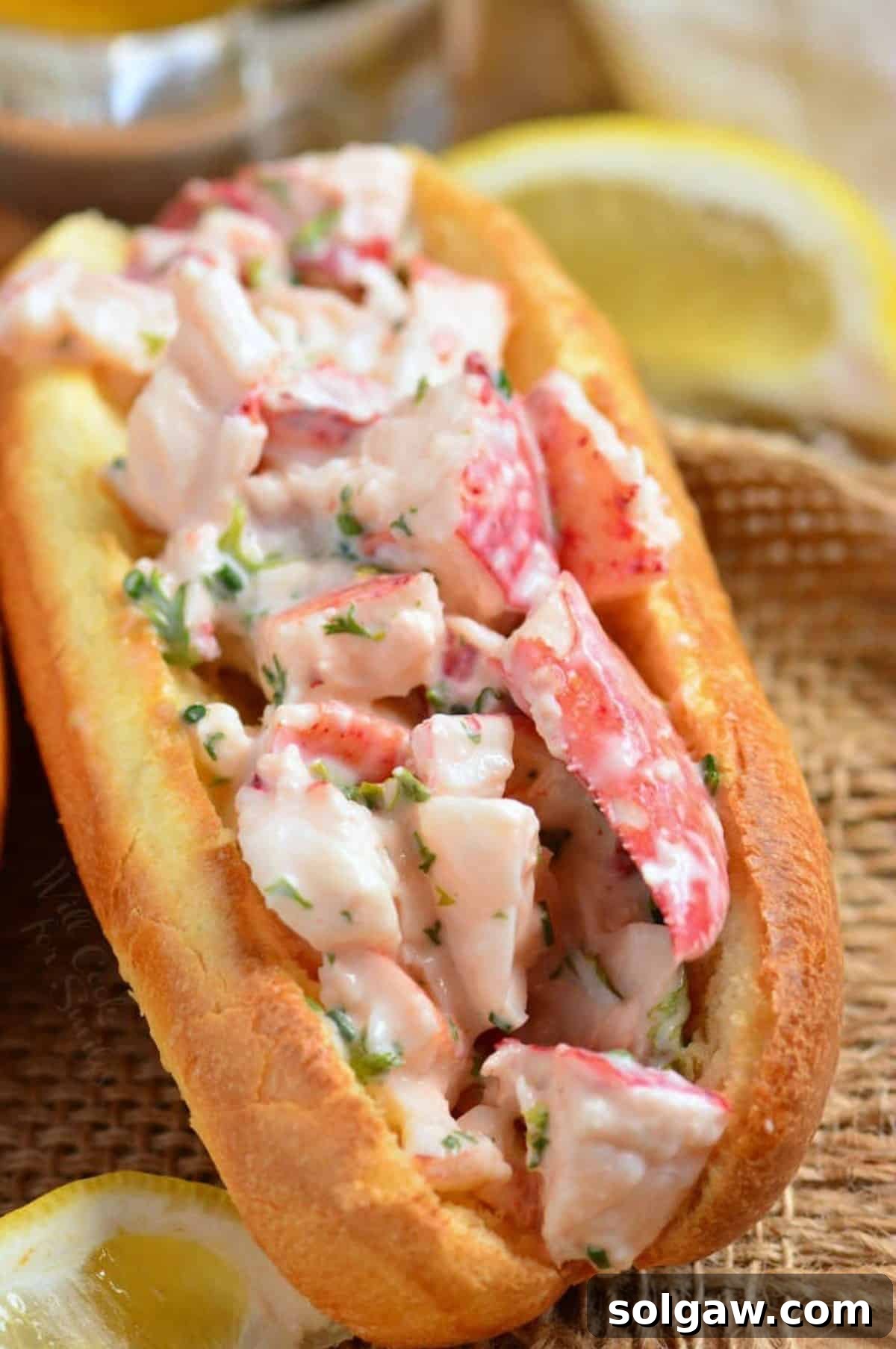 one hot dog bun filled with lump lobster mixture and lemon wedges.