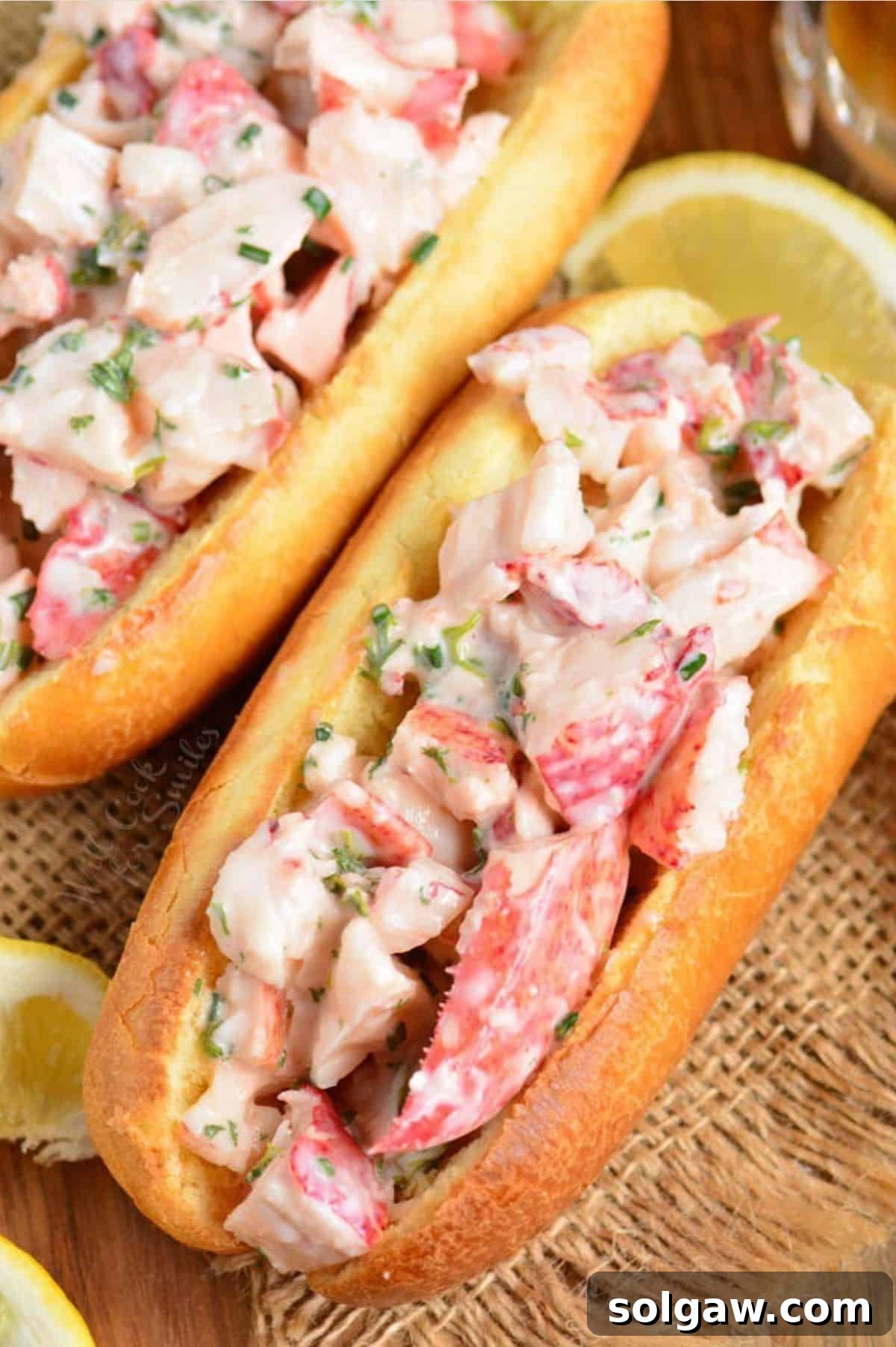 two hot dog buns filled with lobster mixture and lemon wedges.