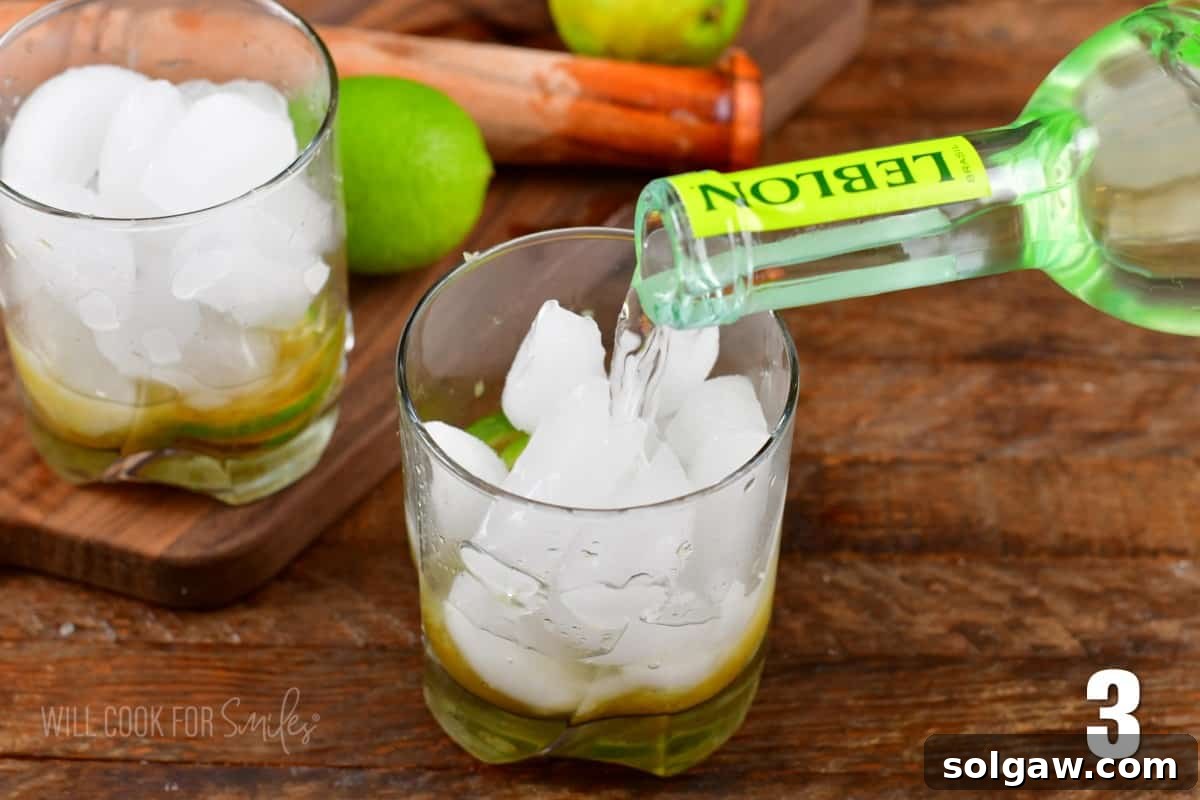 Pouring Cachaca liquor into a short glass filled with ice and muddled limes on a wooden surface.
