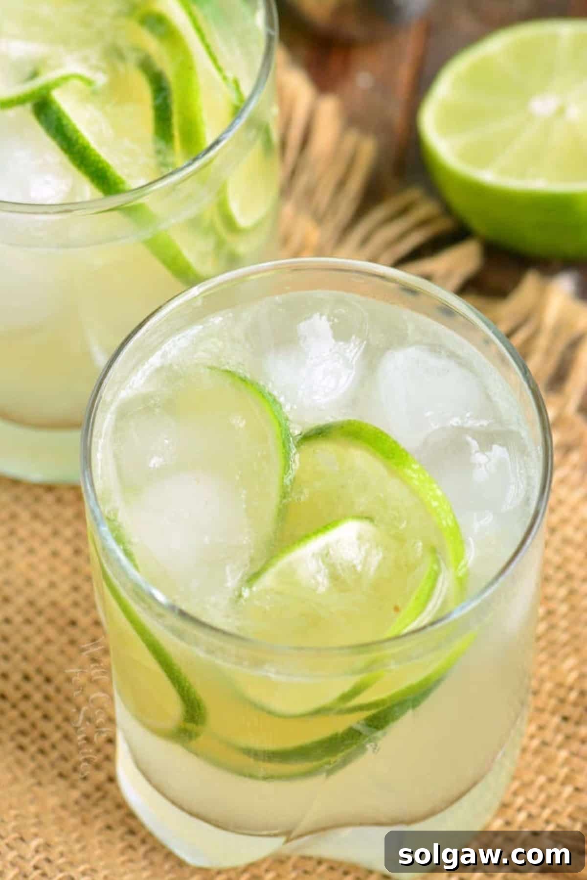A Caipirinha cocktail served in a short glass with ice and lime wedges, presented on a brown tablecloth.