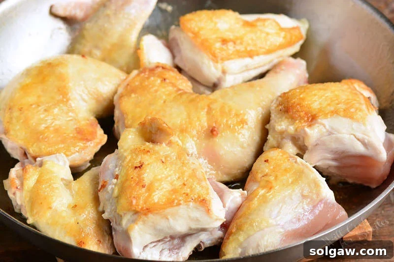 A chef browning chicken pieces in a cast-iron pan, preparing them for the mango sauce