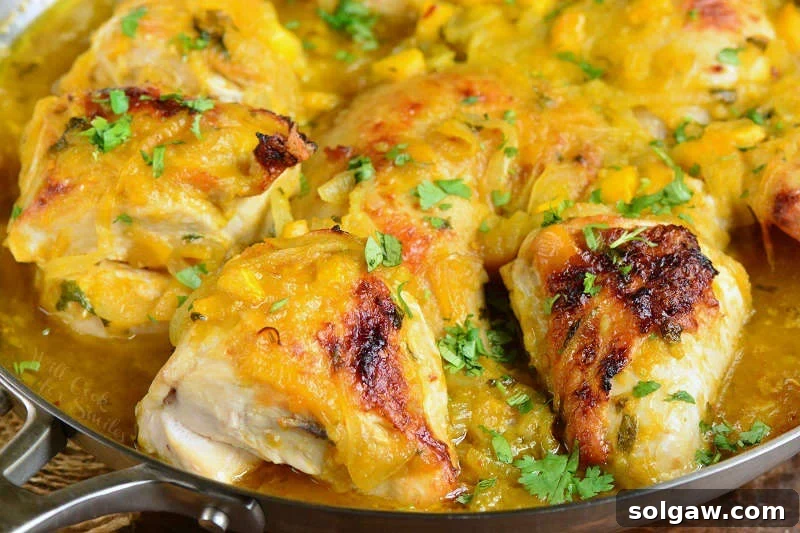 Close-up photo of baked mango chicken sizzling in the pan, with fresh herbs and lime wedges