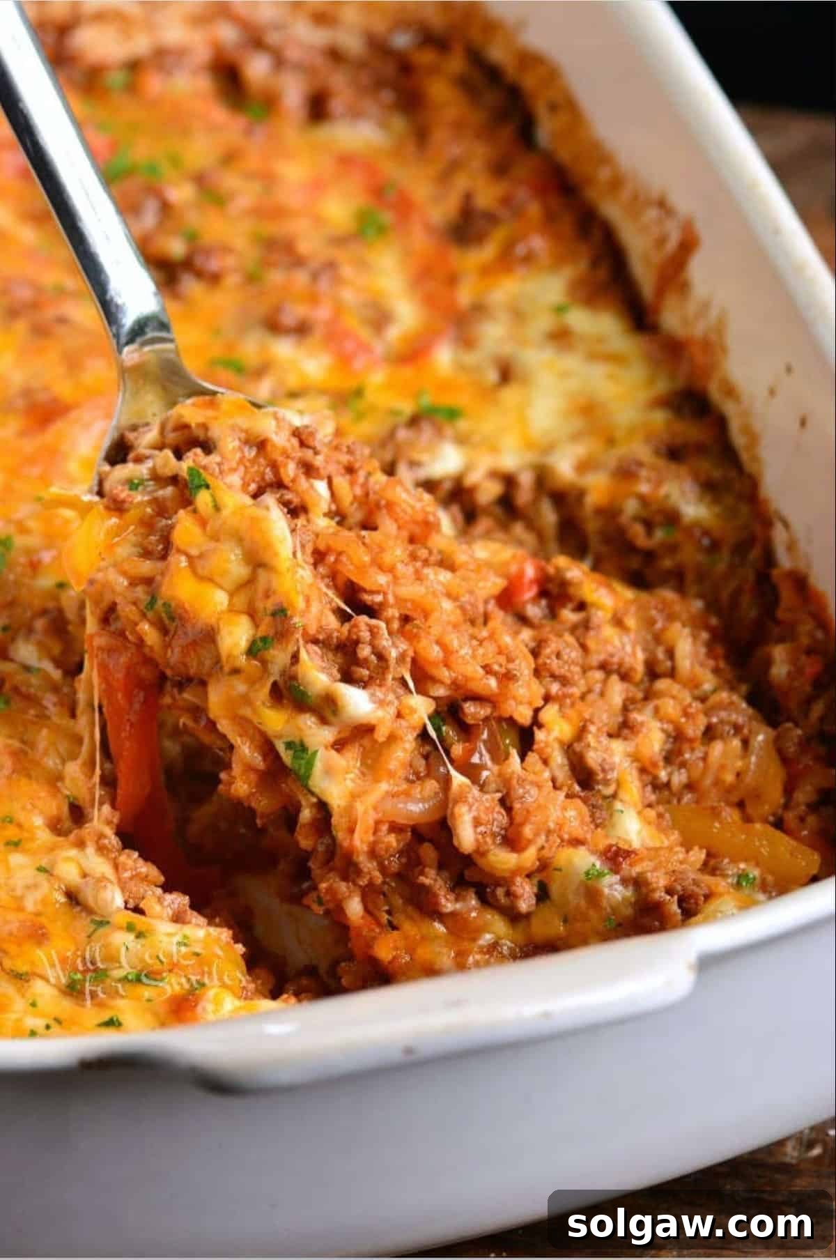 Scooping rice and beef enchilada casserole with a silver serving spoon.