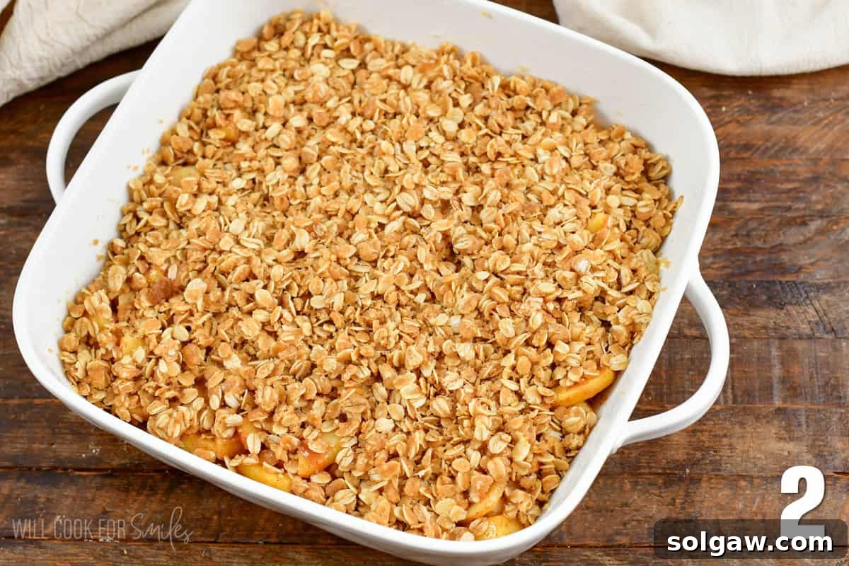 Apple crisp assembled in a baking dish with the oat topping spread evenly over the spiced apple filling.