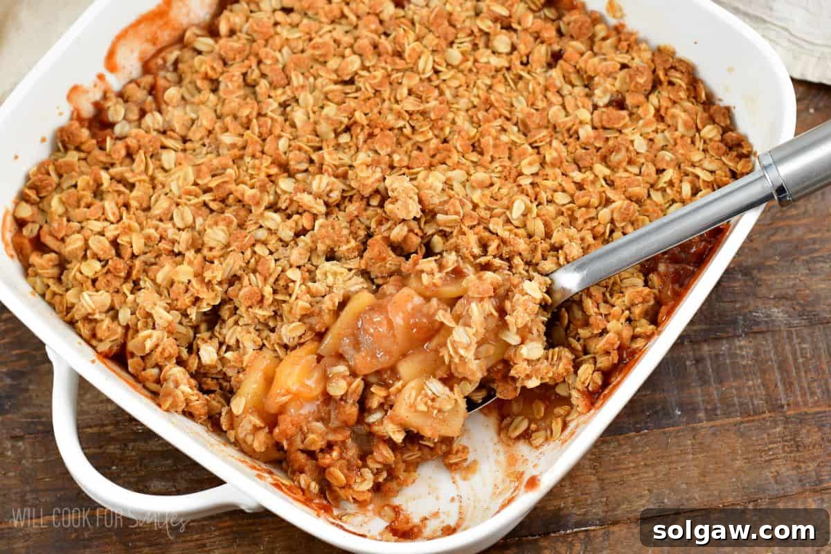 A baking dish of apple crisp with a scoop removed, showcasing the tender apples and crisp topping beneath.