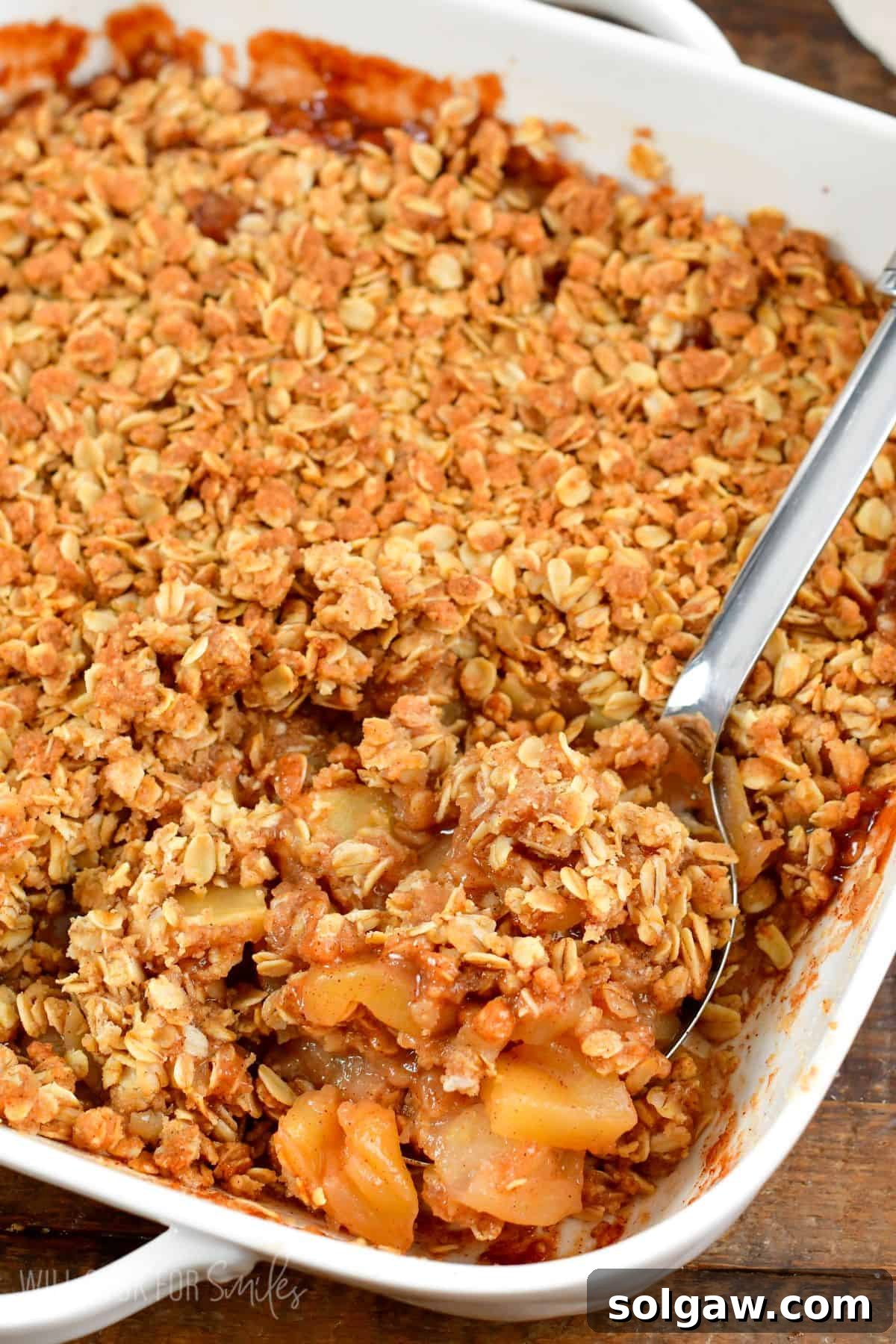 A baking pan filled with golden brown apple crisp, with a spoon having just served a portion.