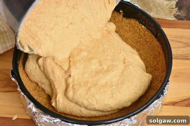 Velvet Sweet Potato Cheesecake 4 Pouring cheesecake filling into a springform pan on a wooden cutting board