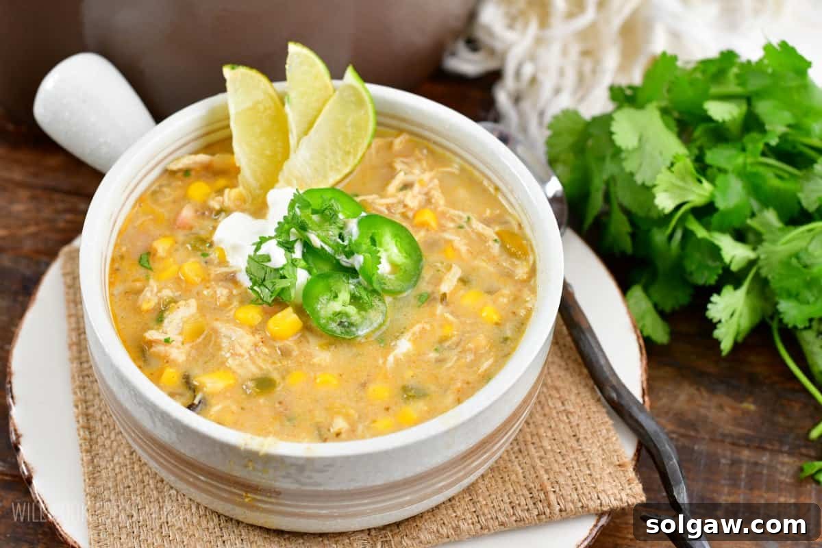 Creamy White Chicken Chili 5 white chicken chili in a bowl with three sliced limes, jalapeno, and sour cream on top.