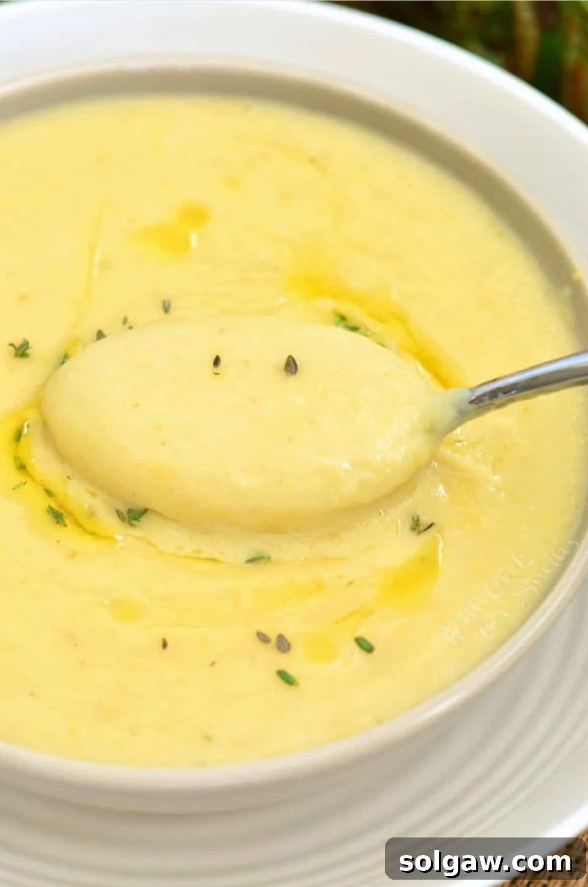 A steaming bowl of creamy potato leek soup with a spoon scooping a portion, garnished with fresh herbs.