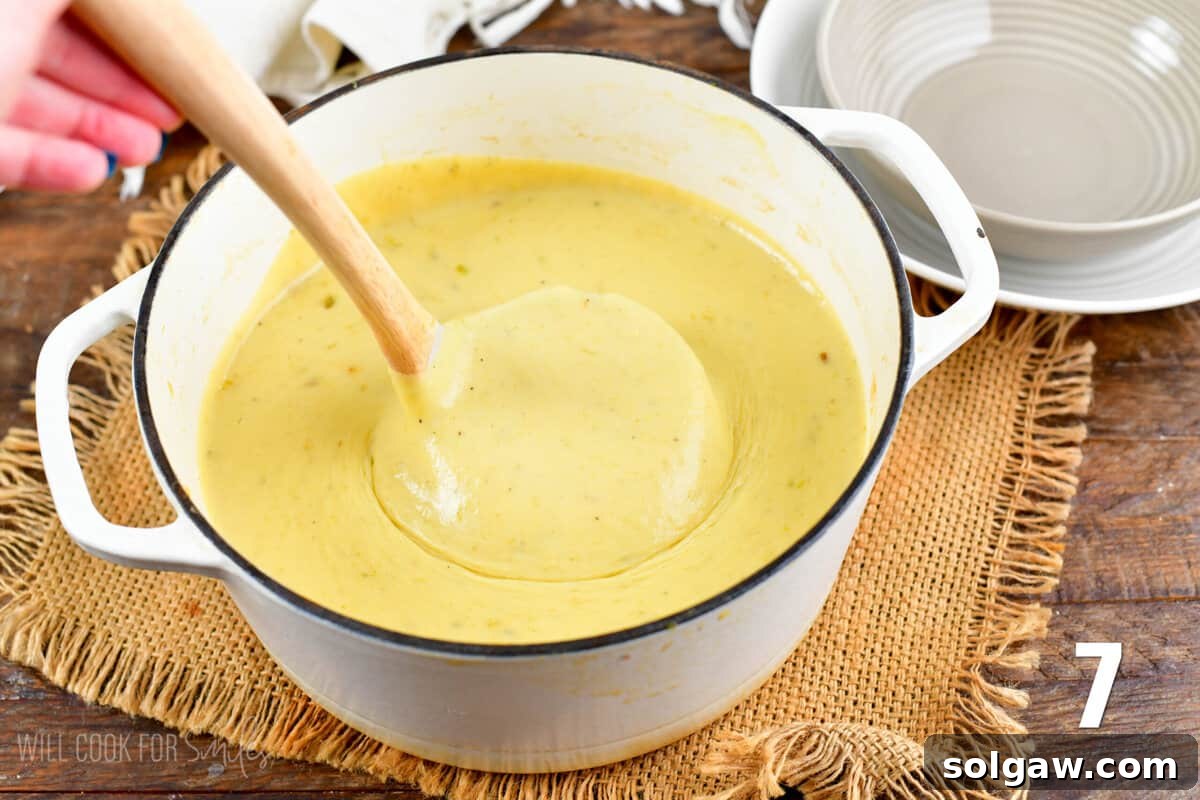 A ladle scooping a generous portion of creamy potato leek soup from a large pot, ready to be served.