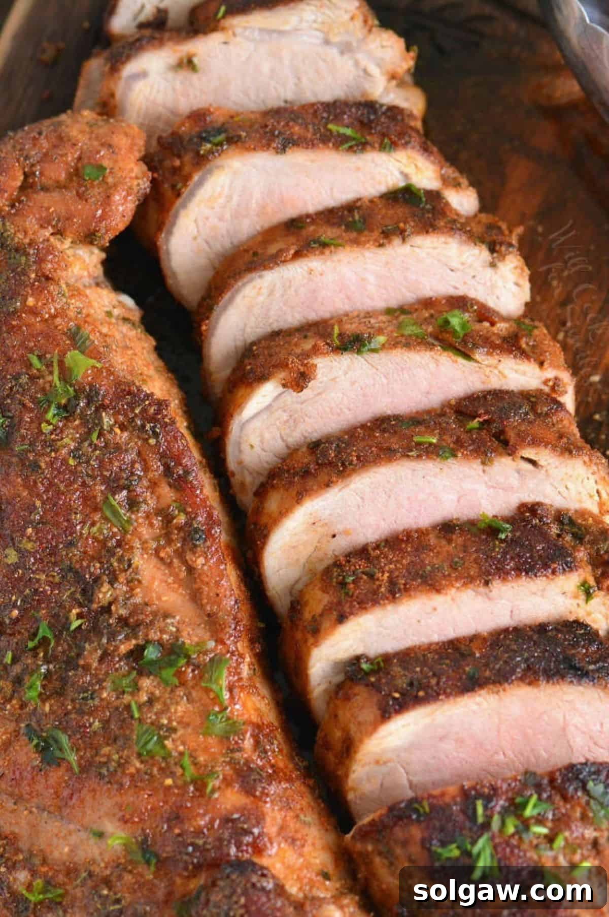 Two sliced roasted pork tenderloin with spice-rub crust and parsley on a wooden platter.