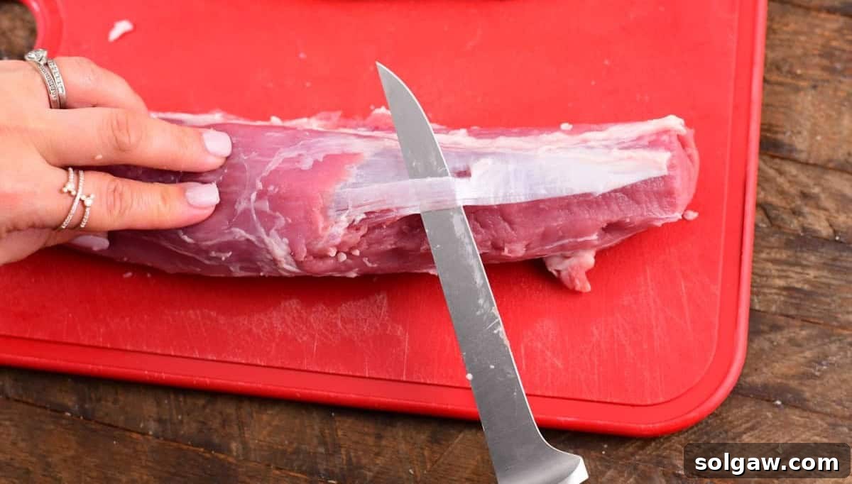 Paring knife removing silverskin from a raw pork tenderloin.