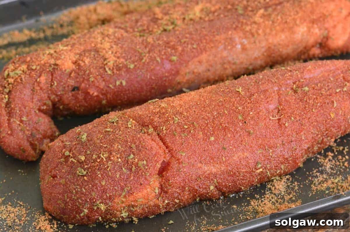 Two uncooked pork tenderloins seasoned and on a baking sheet.