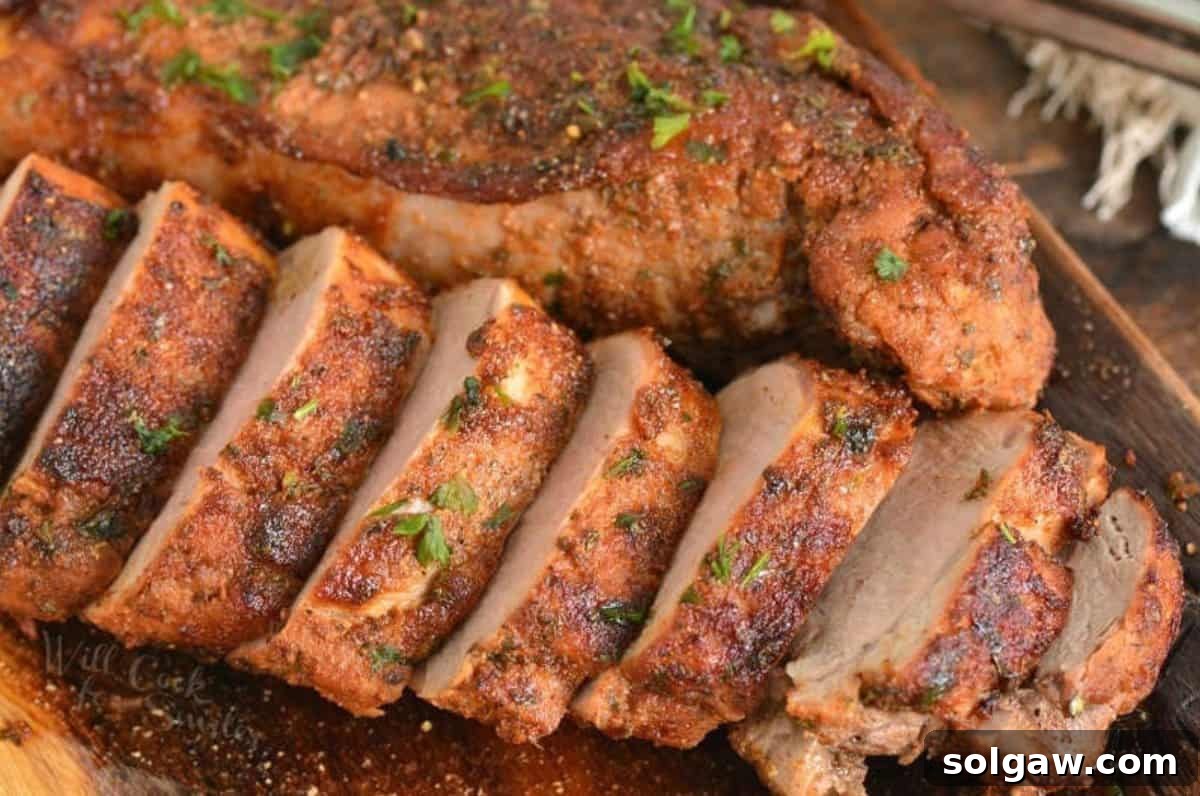 Two roasted pork tenderloins one sliced and one unsliced on a wood cutting board.