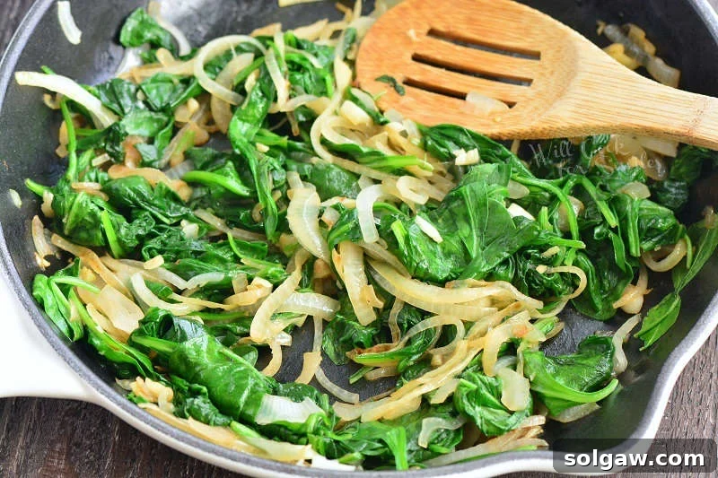 Spinach and onions cooking in a cast iron pan with a wooden spatula