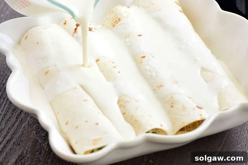 Pouring cream sauce over turkey enchiladas in a casserole dish