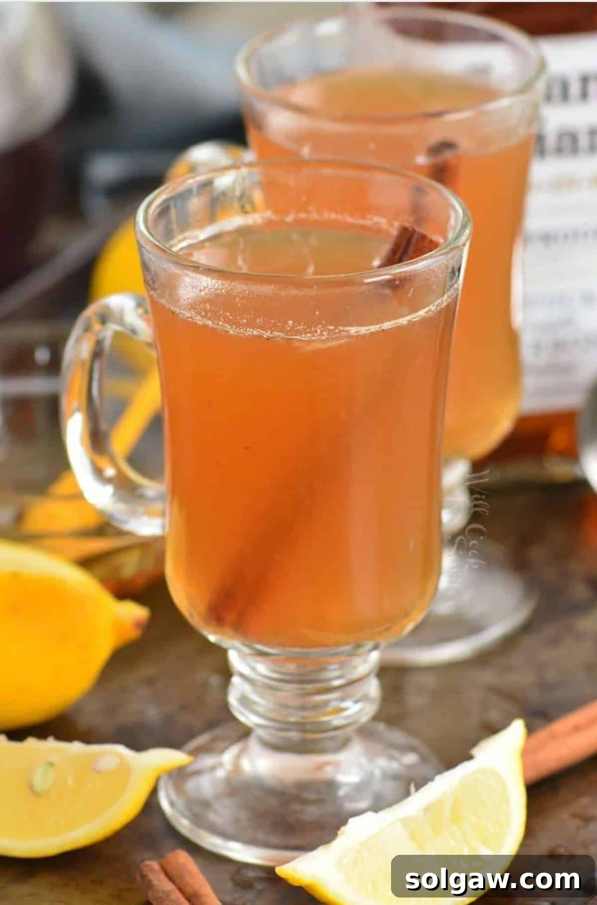 two glass mugs with hot toddies and lemons and cinnamon around.