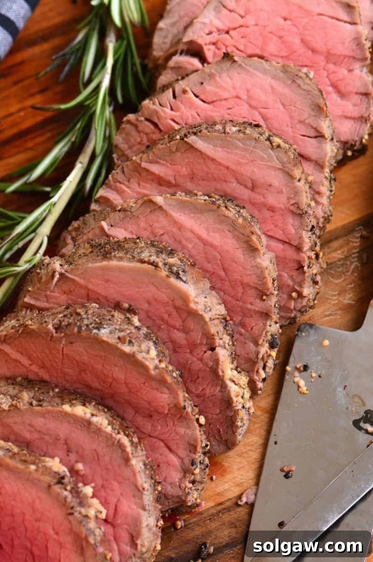 sliced beef tenderloin with seasoning on the sides and rosemary sprig next to it.