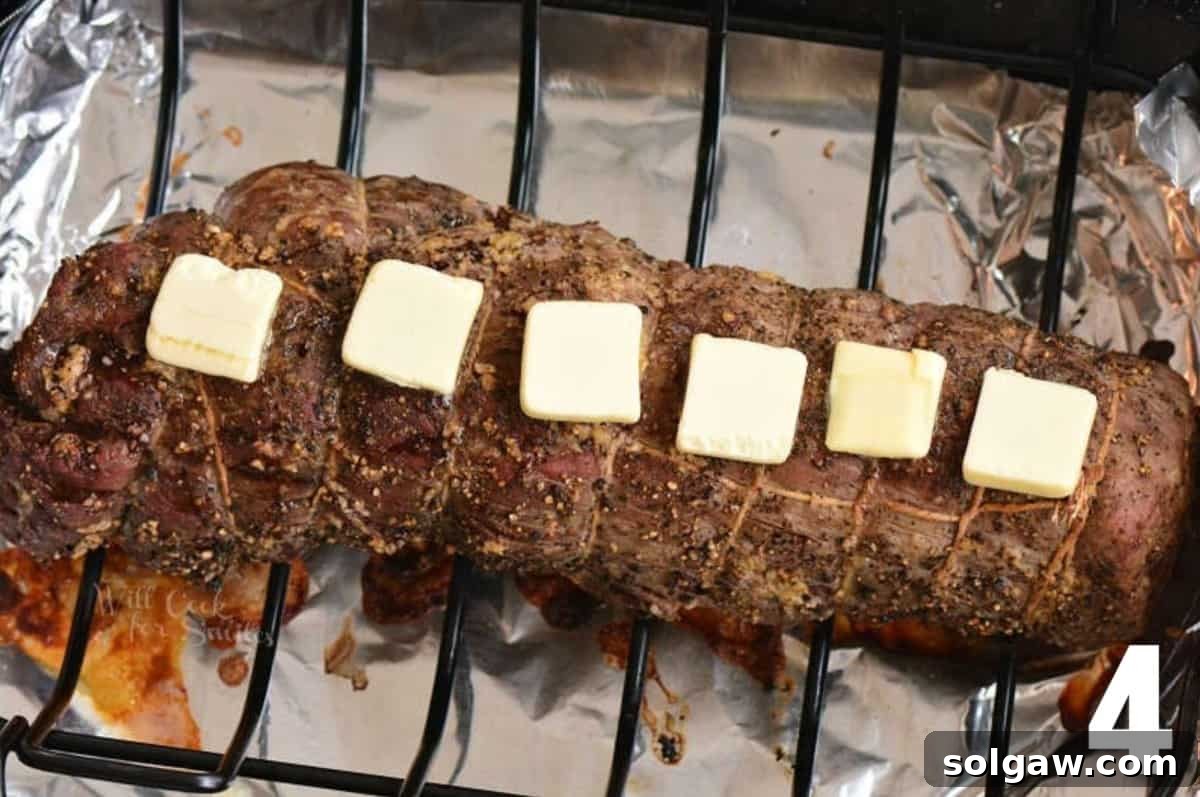 cooked and tied beef tenderloin with butter sliced on top.
