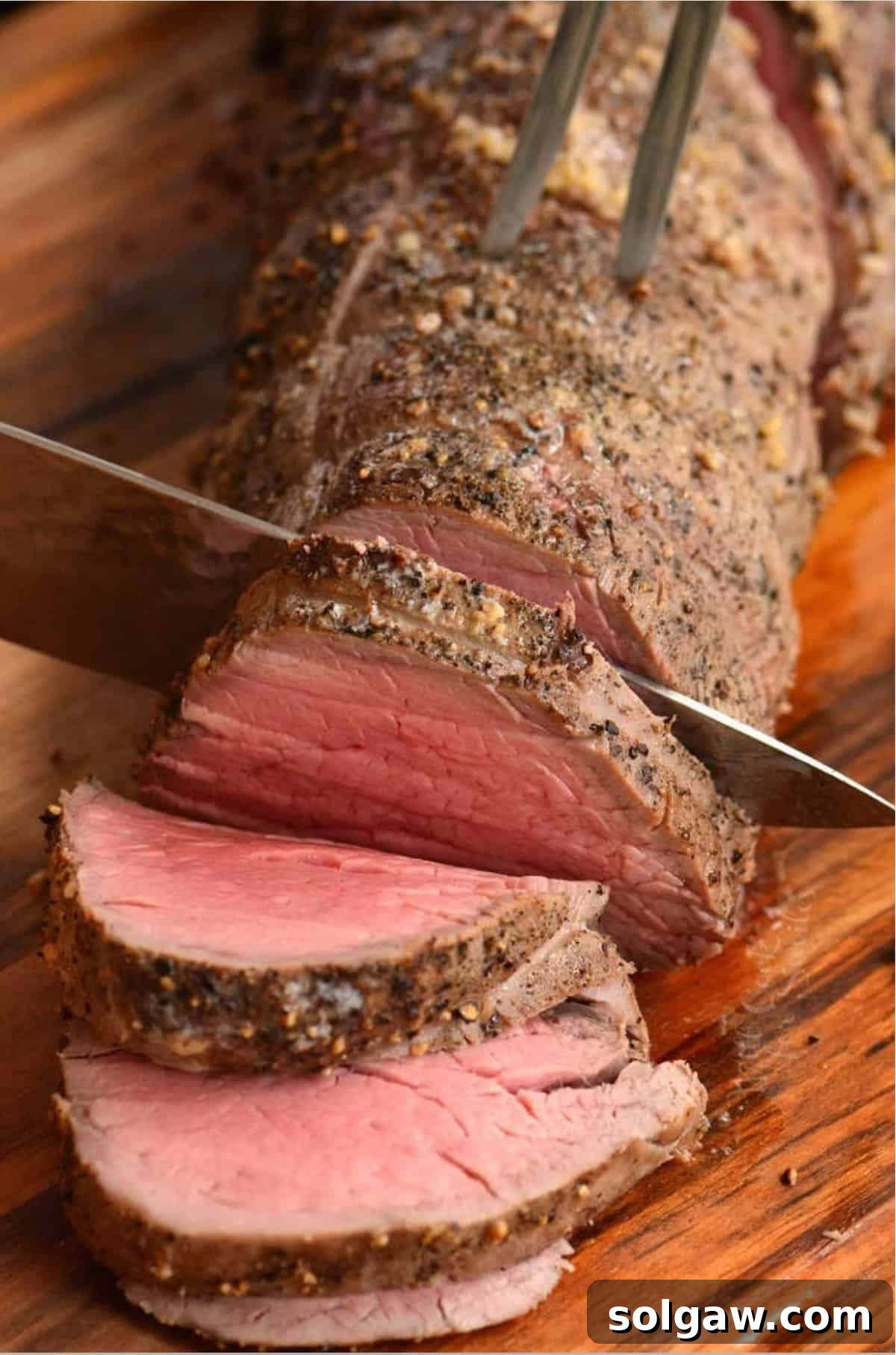 slicing through a beef tenderloin with a knife and a fork.