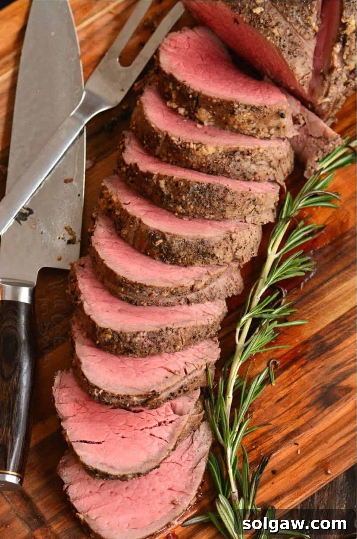 sliced beef tenderloin spread on cutting board next to a knife and rosemary.