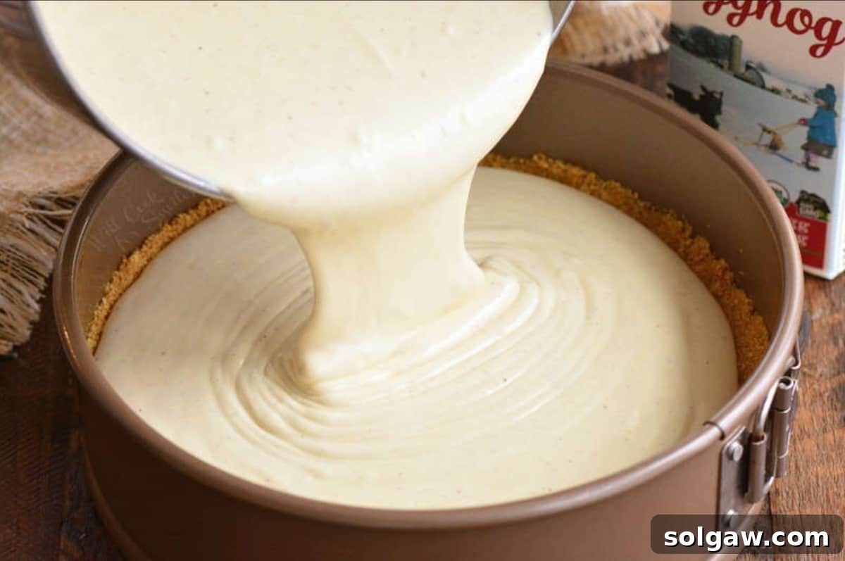Yuletide Eggnog Cheesecake 4 Creamy eggnog cheesecake batter being poured into a foil-wrapped springform pan, showcasing its perfect thick consistency.