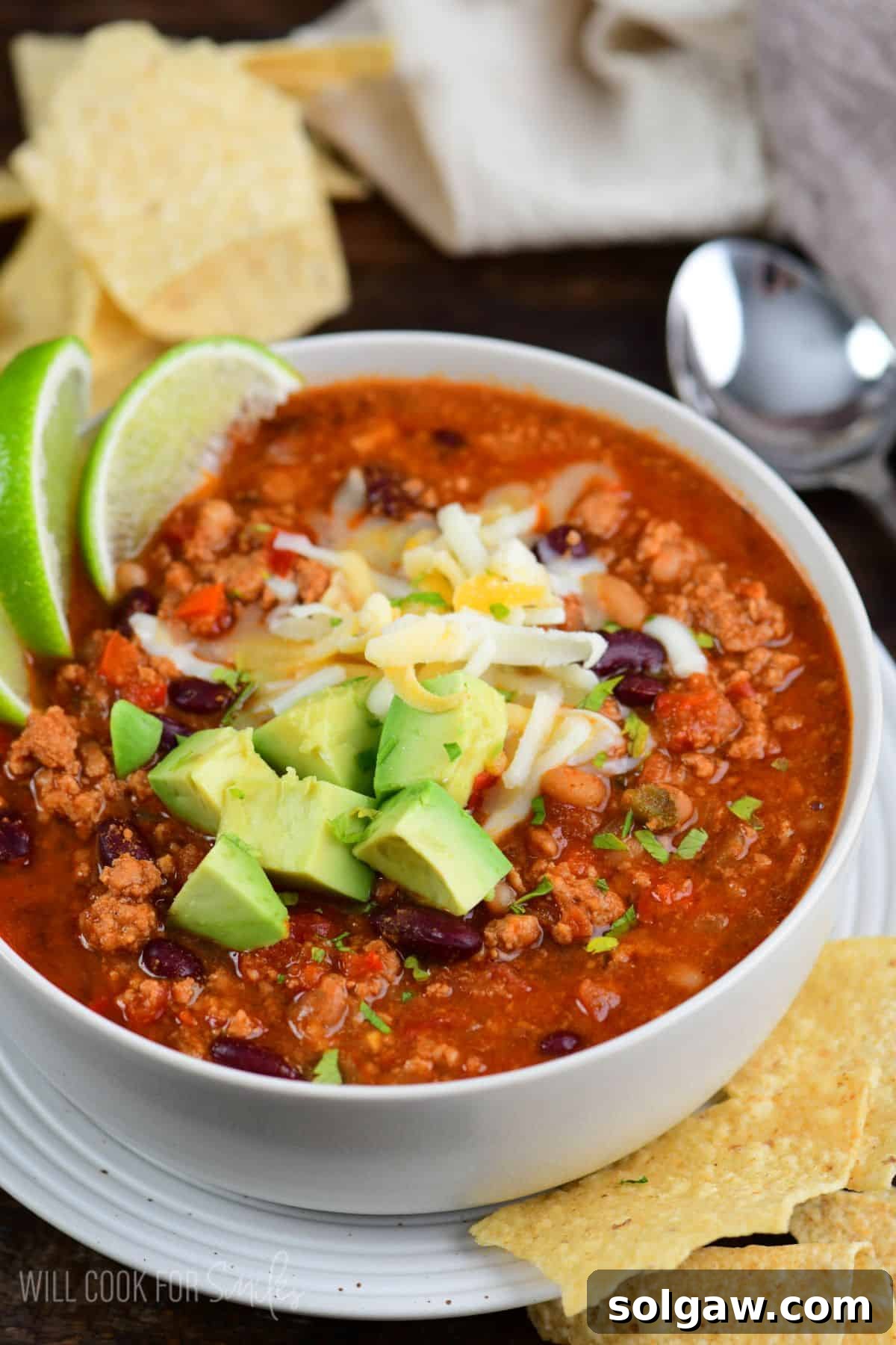 A hearty bowl of turkey chili, garnished with fresh toppings, alongside crunchy tortilla chips.