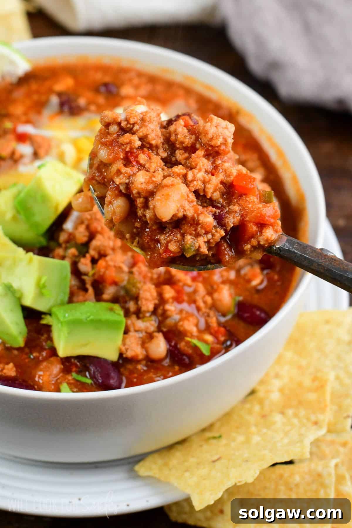 A spoonful of rich turkey chili lifted from a bowl, showcasing its hearty texture.
