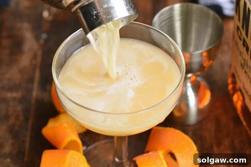 Whiskey Sour Two Takes 8 Pouring the frothy Whiskey Sour with egg white into a chilled glass, showing the creamy texture.