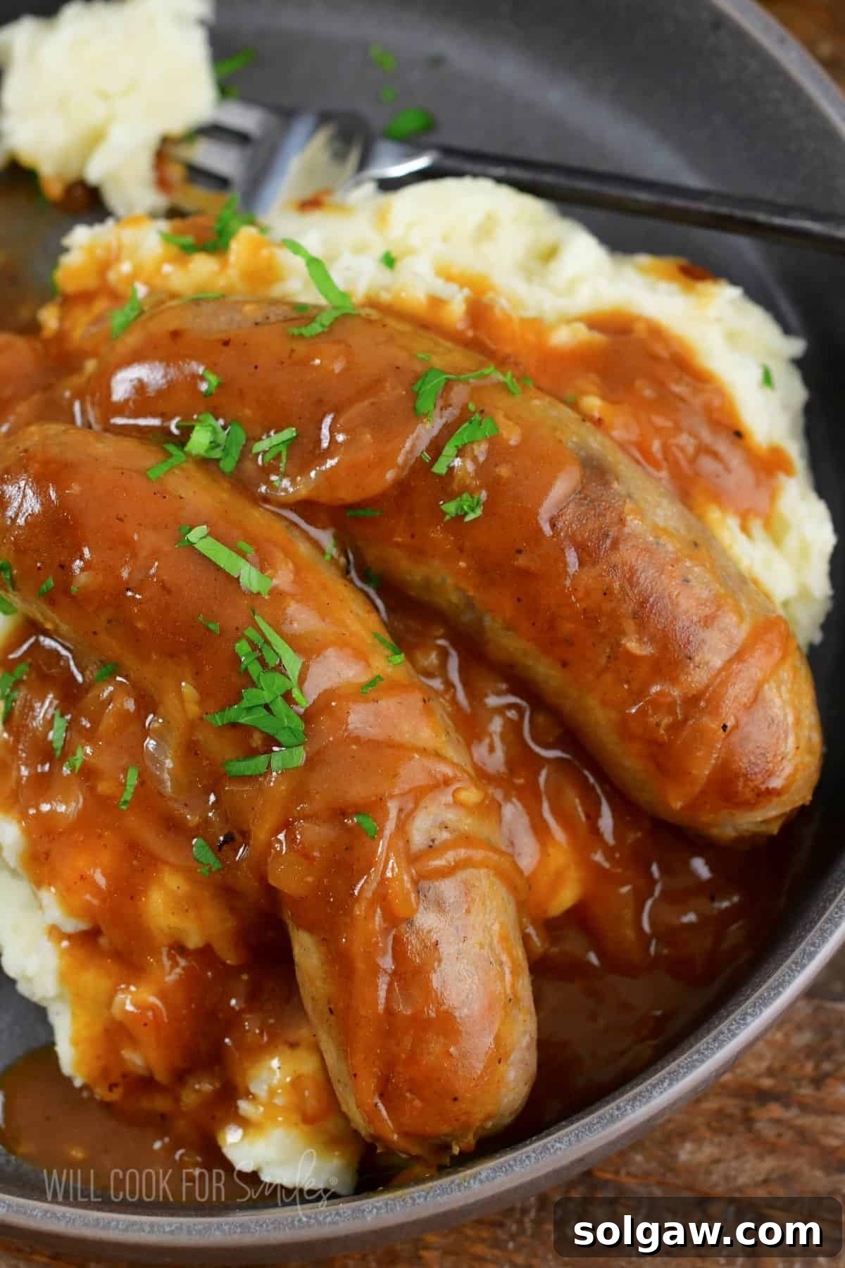 Onion Gravy Smothered Sausages and Mash 2 closeup of sausages in gravy over mashed potatoes.