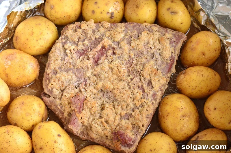 One-Pan Corned Beef with Crispy Potatoes 6 Baby gold potatoes being added around the corned beef brisket in a roasting pan, nestled in the savory pan juices before further cooking.