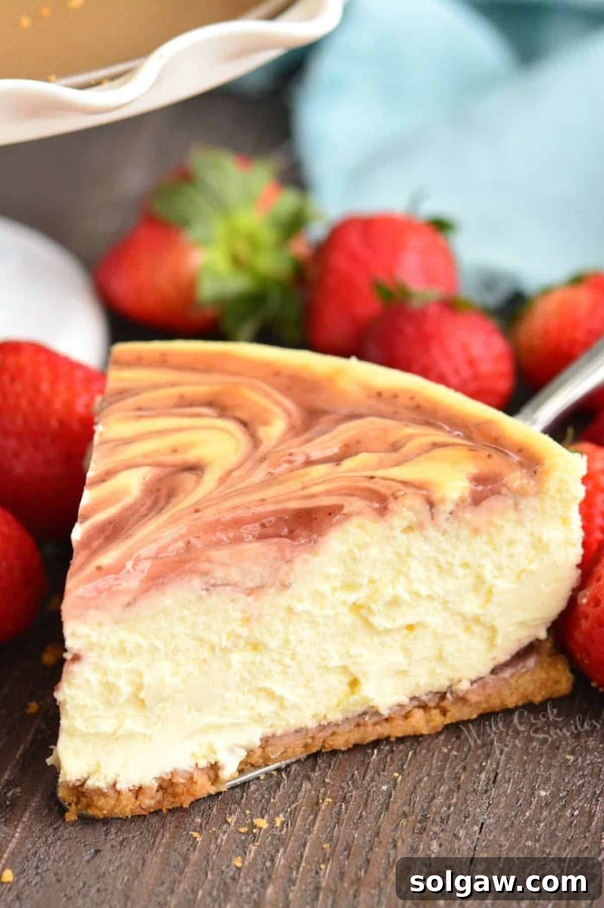 A vibrant slice of strawberry cheesecake, adorned with fresh strawberries, sits invitingly next to a matching cake stand.