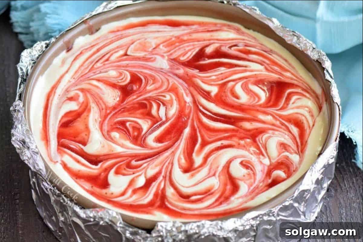 Unbaked cheesecake batter with strawberry sauce swirled in, ready for baking.