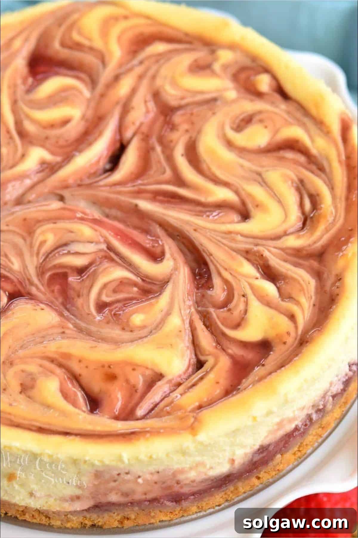 A baked strawberry swirled cheesecake on an elegant cake plate, showcasing its vibrant patterns.