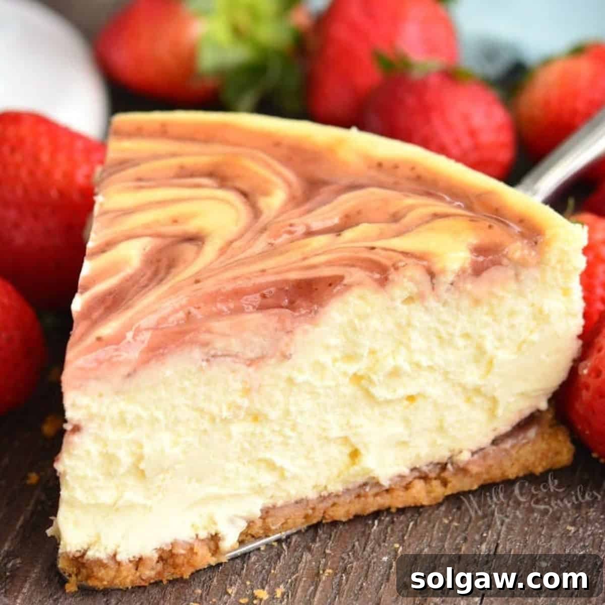 A luscious slice of strawberry cheesecake on a silver spatula, surrounded by fresh strawberries.