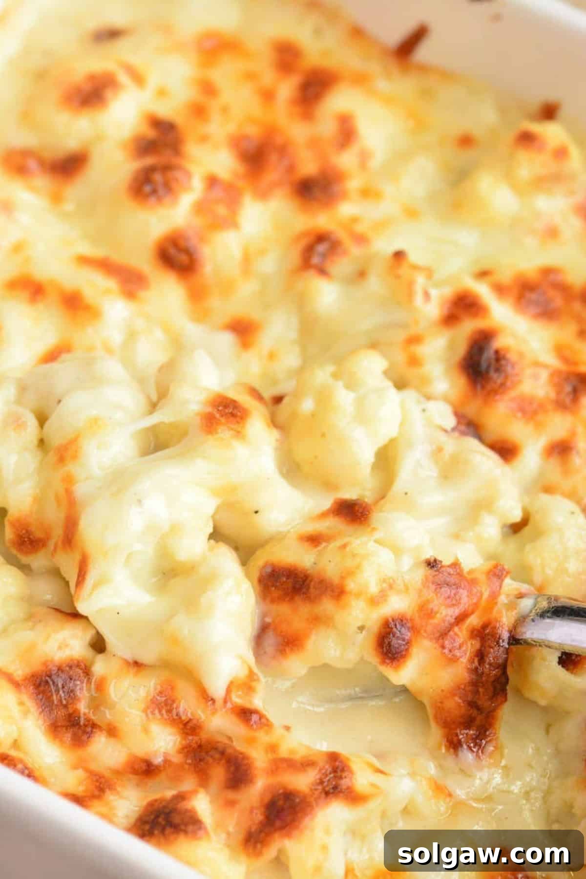 Creamy Cauli Mac 2 Scooping Cauliflower mac and cheese out of a baking dish.