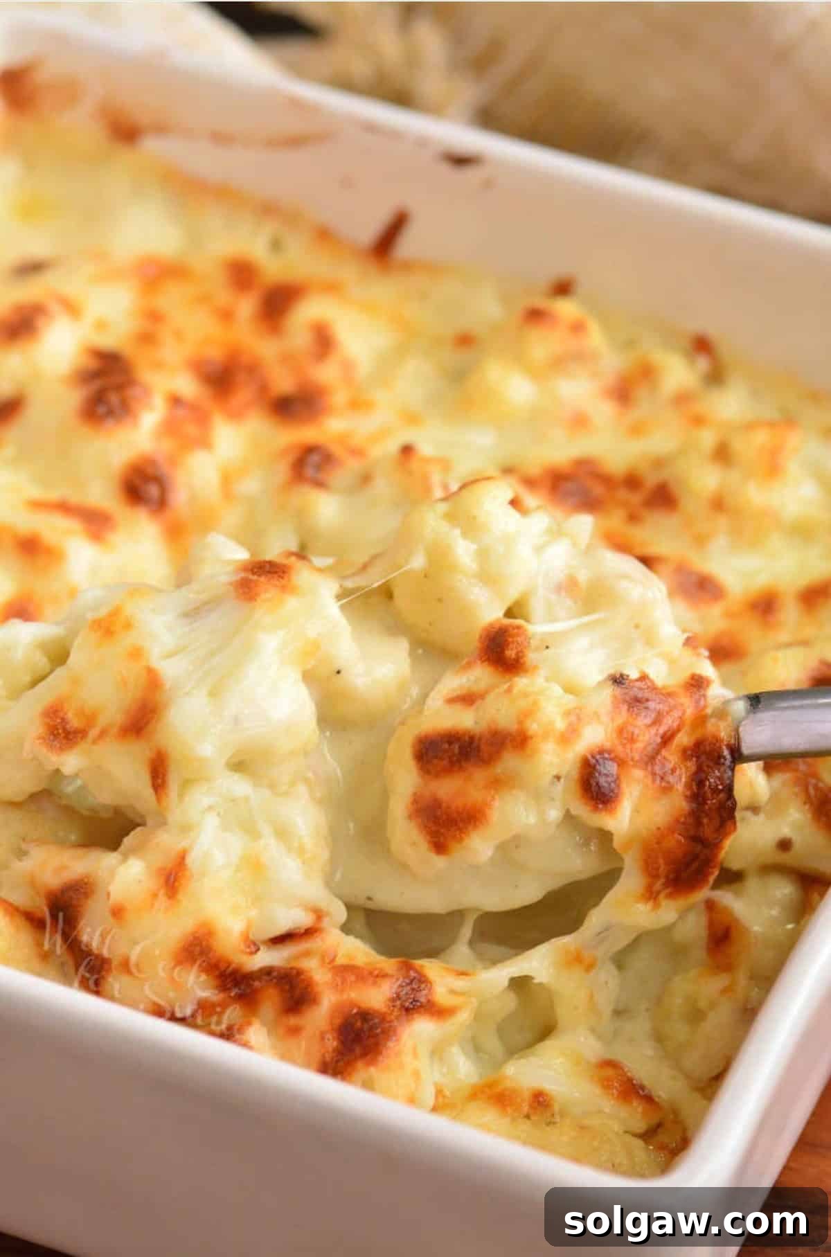 Creamy Cauli Mac 5 Scooping cauliflower mac and cheese out of a baking dish.